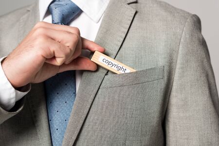 cropped view of businessman putting wooden block with word copyright in pocket isolated on grey