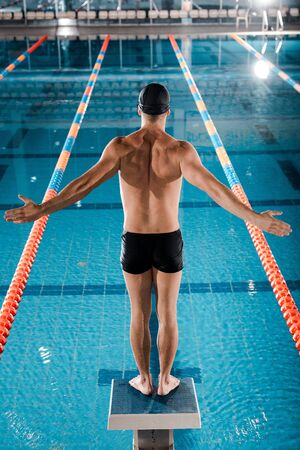 back view of swimmer standing with outstretched hands near swimming poolの写真素材