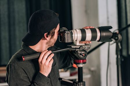 Side view of handsome videographer with camera on tripod in photo studioの写真素材
