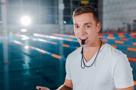 cheerful trainer holding whistle in mouth while looking at cameraの写真素材