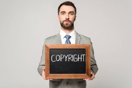 confident businessman holding chalkboard with copyright lettering isolated on grey