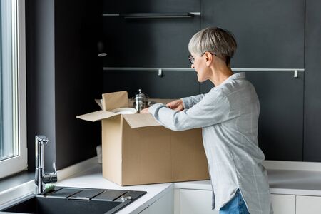 mature woman in glasses unpacking box in new house
