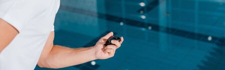 panoramic shot of sportsman holding timer near swimming poolの写真素材