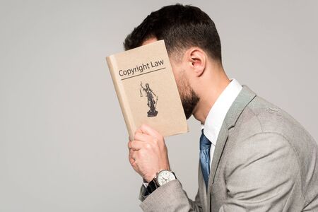 side view of lawyer obscuring face with copyright law book isolated on greyの写真素材