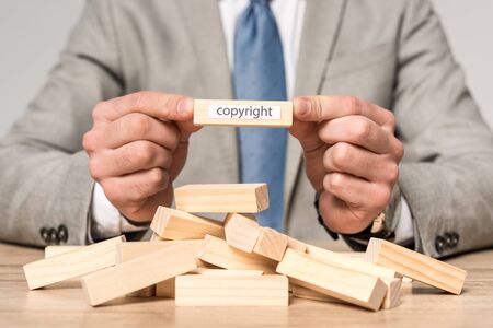 partial view of businessman holding wooden block with copyright inscription isolated on greyの写真素材
