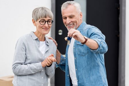 mature man holding keys of new house and smiling woman looking at it