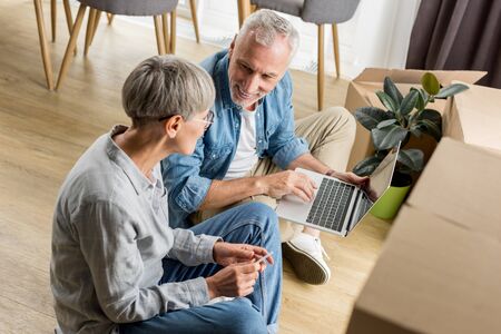 high angle view of mature man with laptop talking with woman in new houseの写真素材