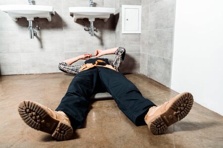 installer holding pliers while lying on floor in bathroomの写真素材