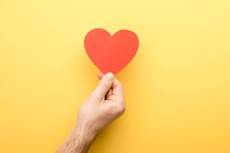cropped view of man holding heart-shaped card on yellow backgroundの写真素材