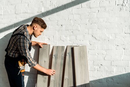 side view of handsome installer standing near wooden shelvesの写真素材