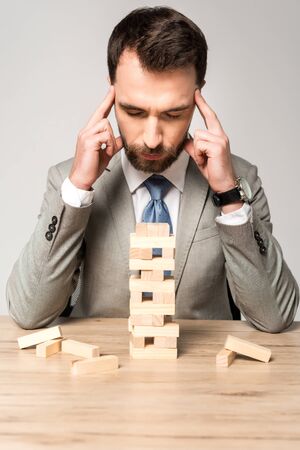 thoughtful businessman sitting with closed eyes near blocks wood game isolated on grey