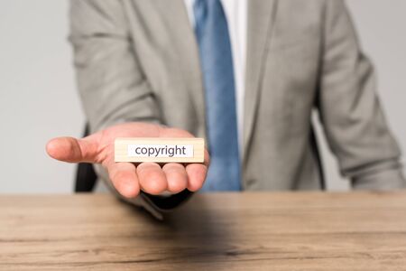 cropped view of businessman holding wooden block with copyright inscription isolated on greyの写真素材