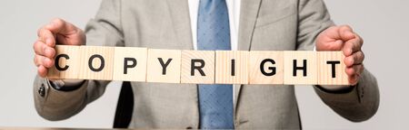 partial view of businessman holding wooden cubes with word copyright isolated on grey, panoramic shotの写真素材