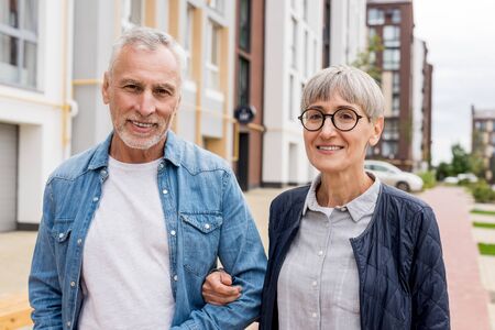 mature man and smiling woman looking at camera near new buildingsの写真素材