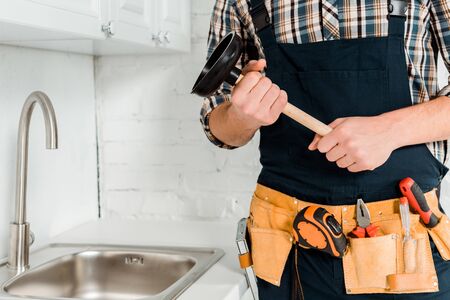 cropped view of plumber holding plunger near sink in kitchenの写真素材