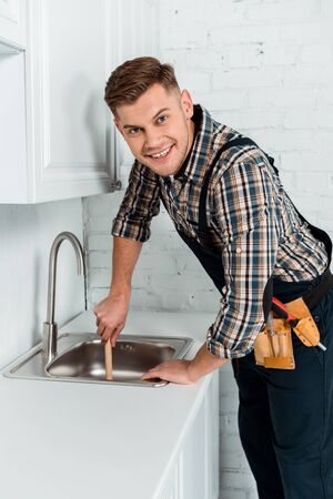 happy installer holding plunger near sink in kitchenの写真素材