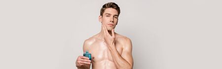 sexy man with muscular torso applying aftershave on face isolated on grey, panoramic shotの写真素材