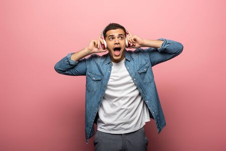 Shocked man in headphones looking away on pink background