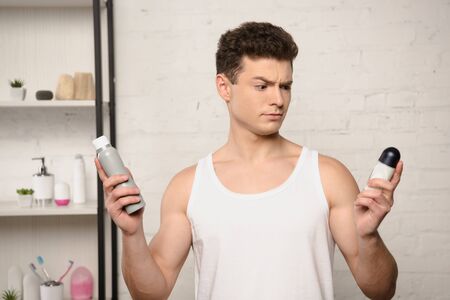 skeptical young man in white sleeveless shirt holding deodorantsの写真素材