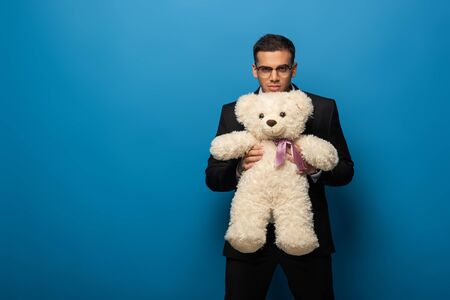 Young businessman with teddy bear looking at camera on blue backgroundの写真素材