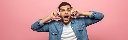 Panoramic shot of excited man in headphones listening music isolated on pink