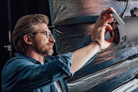 bearded art director touching reflector in photo studio