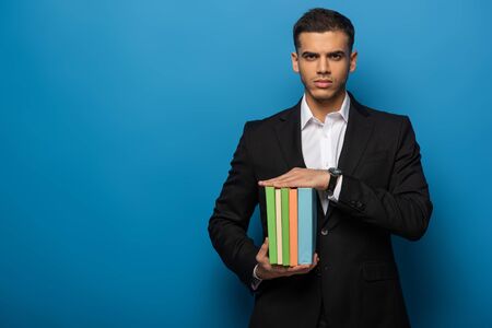 Handsome businessman holding colored books on blue background