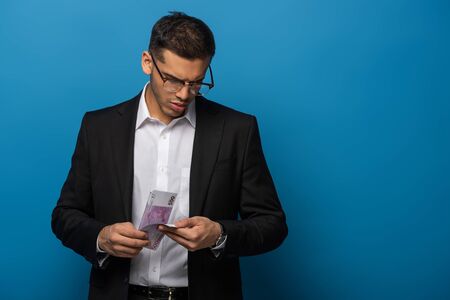 Young businessman counting euro banknotes on blue background
