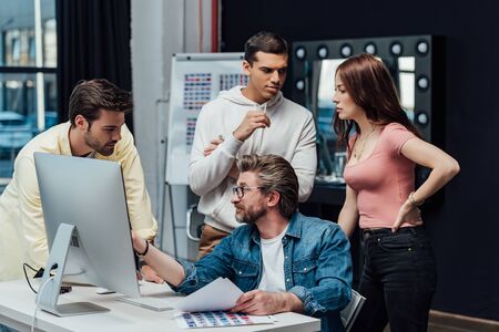 creative director in glasses looking at assistant near computer monitor