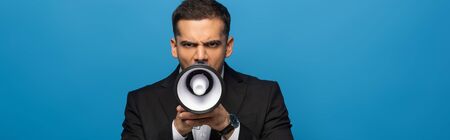 Panoramic shot of businessman screaming in loudspeaker isolated on blueの写真素材