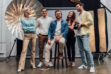 panoramic shot of happy team smiling while looking at camera in photo studio