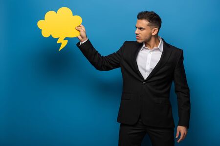 Side view of angry businessman looking at speech bubble on blue background