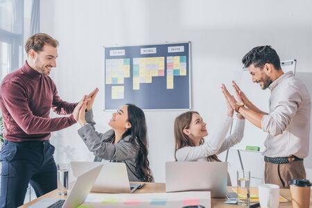 cheerful multicultural businesswomen and businessmen giving high five in office