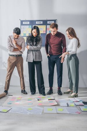 multicultural scrum masters posing and looking at sticky notes on floorの写真素材