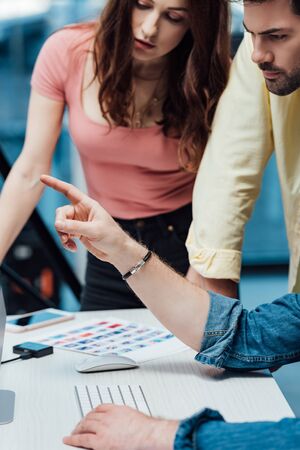 cropped view of art director pointing with finger near coworkers