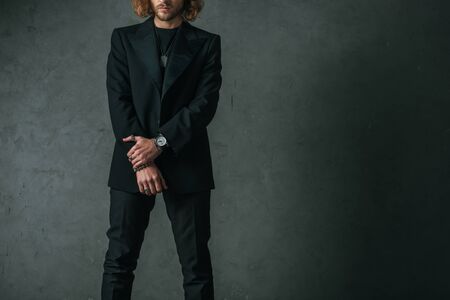 cropped view of fashionable businessman in black suit posing in dark near grey wallの写真素材