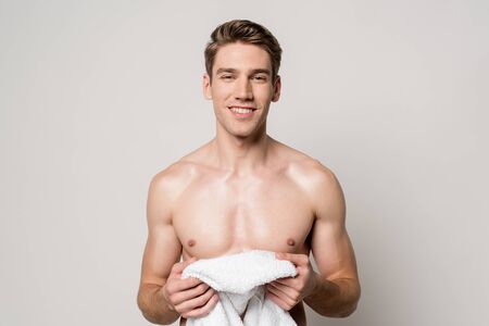 smiling sexy young naked man holding cotton towel isolated on greyの写真素材