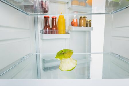 Selective focus of bitten apple with sauces on open fridge door isolated on whiteの写真素材