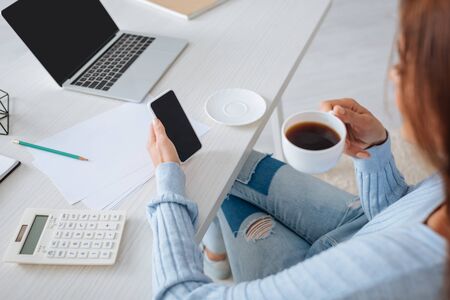 selective focus of woman holding smartphone with blank screen and cup with coffee while relaxing at homeの写真素材