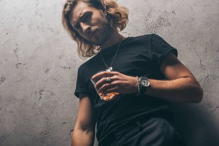 low angle view of fashionable businessman in black outfit with whiskey near grey wallの写真素材