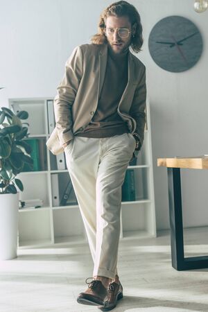 elegant fashionable businessman walking with hands in pockets in sunlight in officeの写真素材