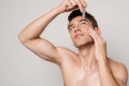 sexy man with bare torso using eye drops isolated on greyの写真素材