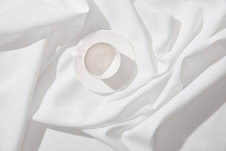 Top view of empty coffee cup with saucer on white wavy tableclothの写真素材