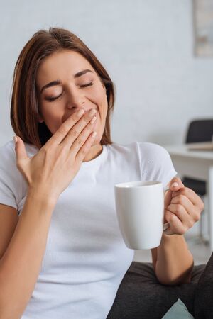 tired girl yawning and cover mouth while holding cupの写真素材