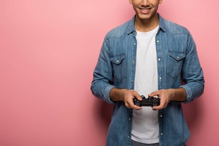 Cropped view of smiling man holding gamepad on pink background