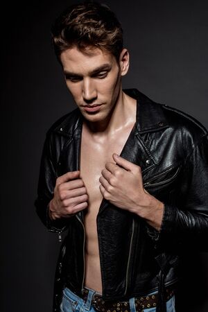 sexy young man with muscular torso in biker jacket and jeans on black backgroundの写真素材