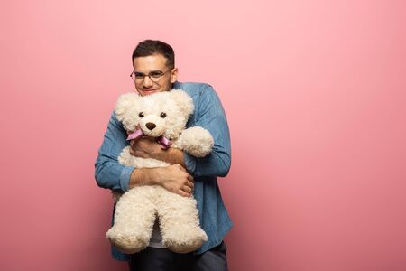 Handsome smiling man hugging teddy bear and looking at camera on pink backgroundの写真素材