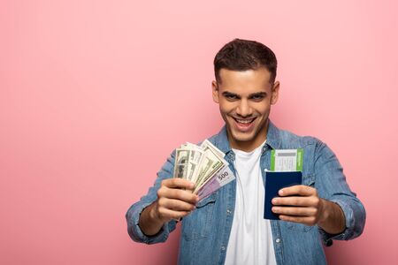 Man holding passport with boarding pass and cash while smiling at camera on pink background