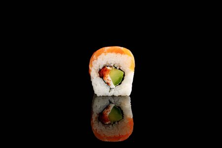 fresh delicious Philadelphia sushi piece with avocado, creamy cheese, salmon and masago caviar isolated on blackの写真素材