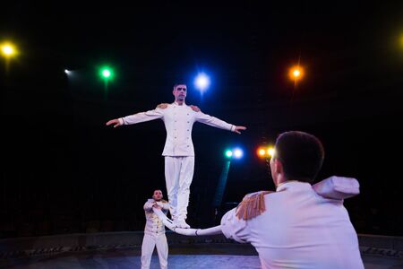 selective focus of handsome acrobat balancing on pole near men in circus